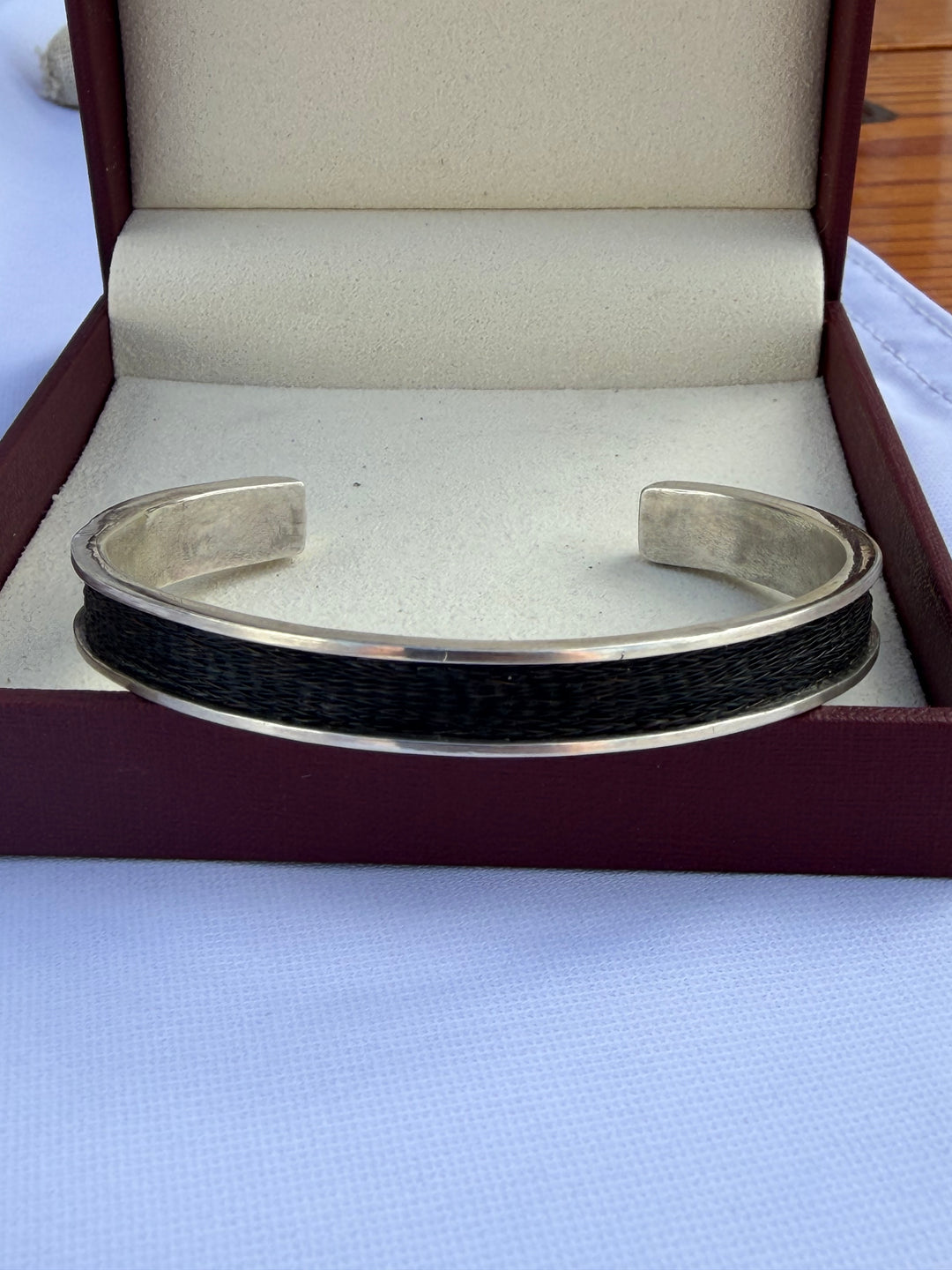 sterling silver cuff with woven horsehair set into it sitting inside of a wine red verstara box with cream lining
